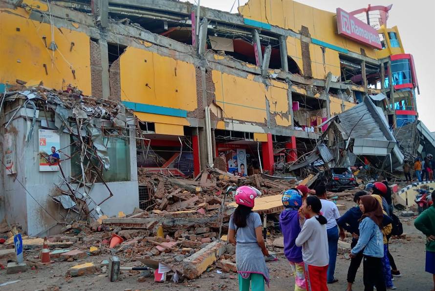 Residents stand in front of a damaged shopping mall after an earthquake hit Palu