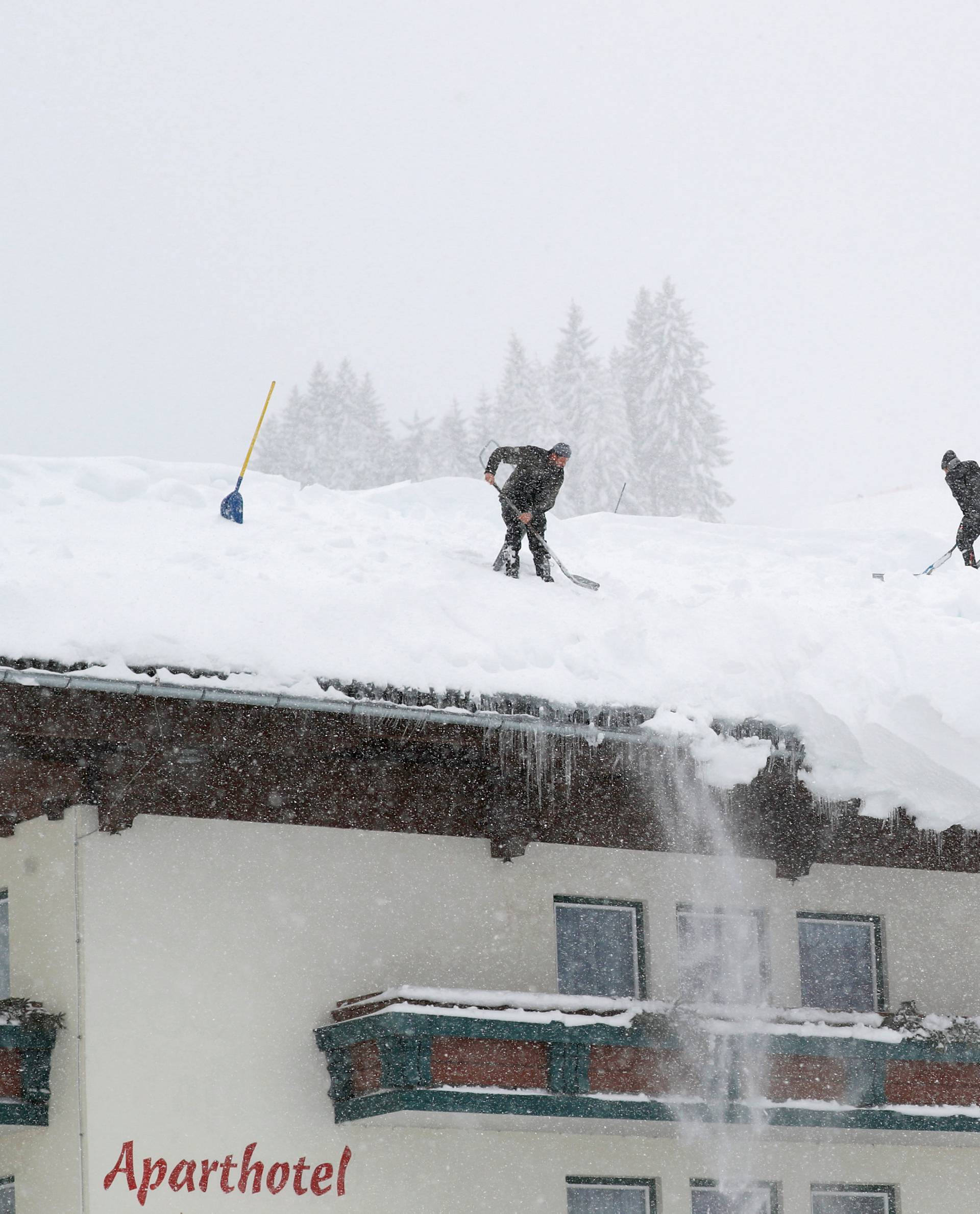Two men shovel snow on a rooftop during heavy snowfall in Filzmoos