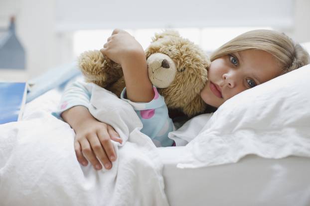 Sick girl laying in bed with teddy bear