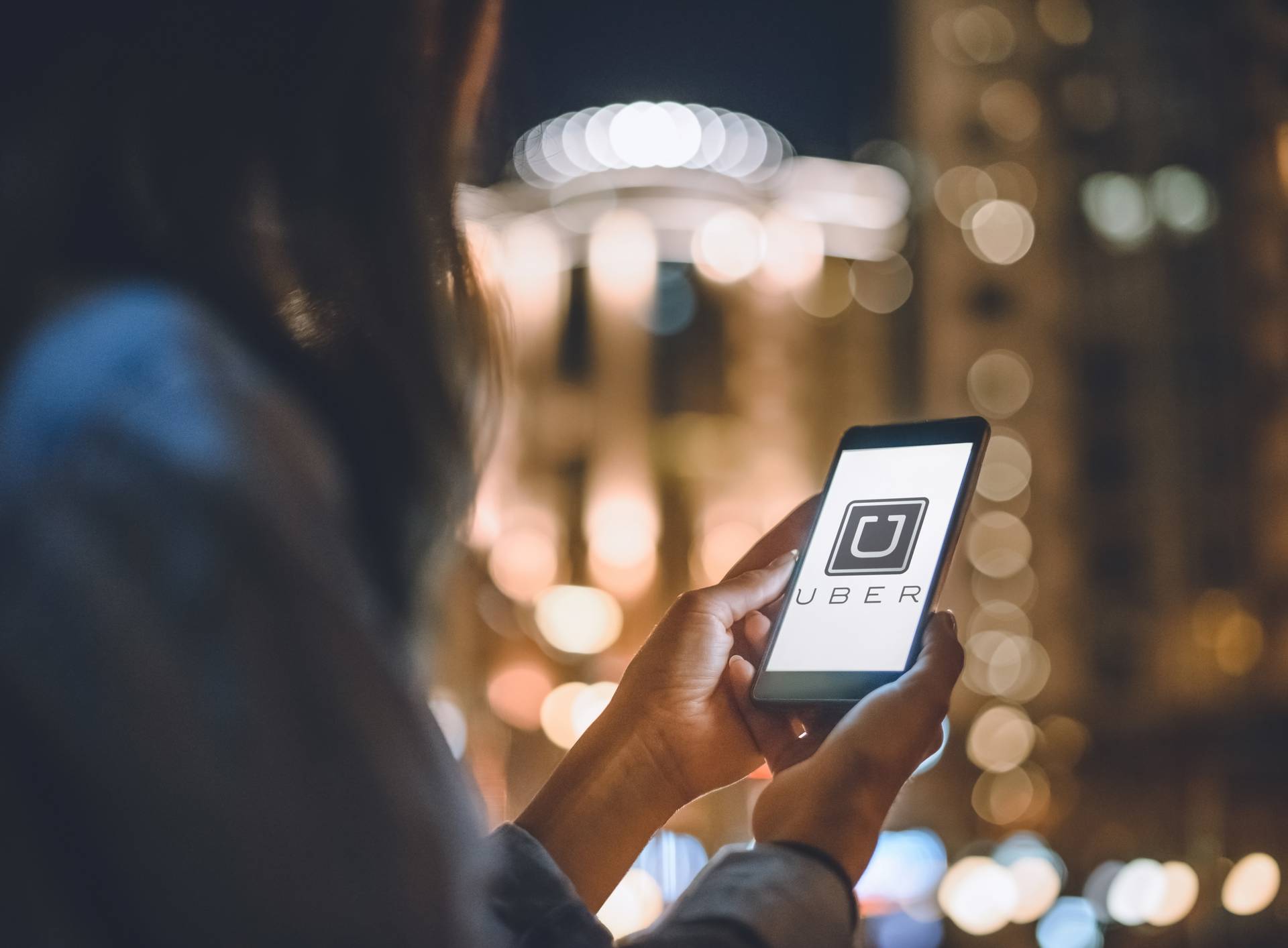 partial view of woman using smartphone with uber logo on screen and night city lights on background