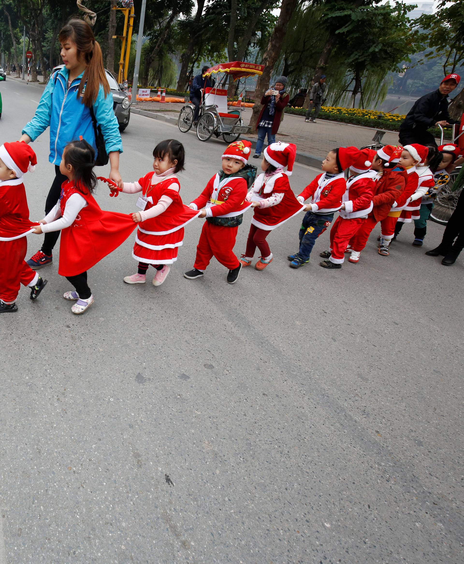 Children wearing Santa Claus outfits cross a street in Hanoi, Vietnam