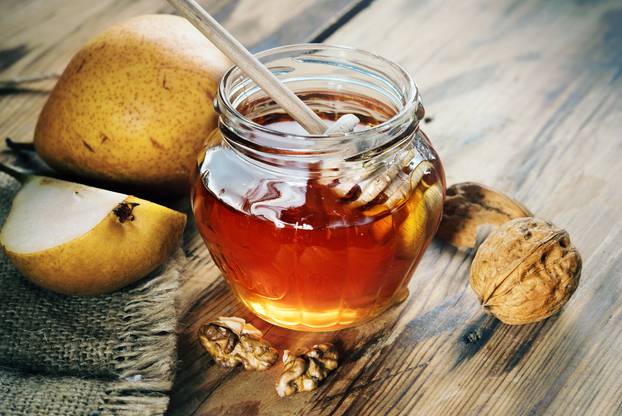 Jar of honey on a wooden table with walnuts and fruit