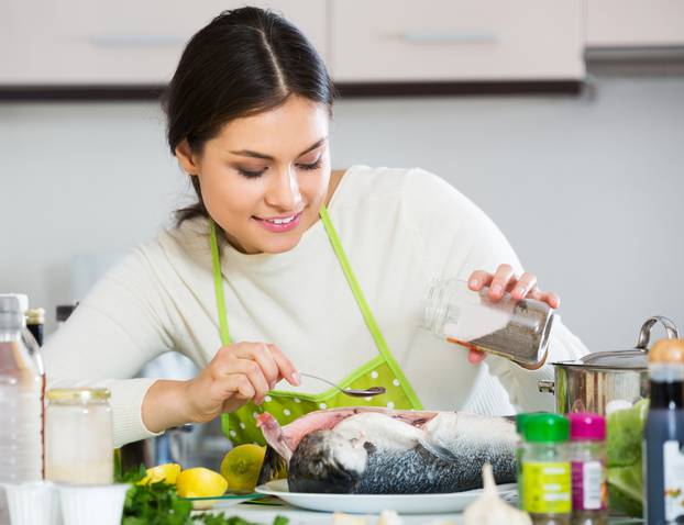 Young woman salting down fresh salmon fish in kitchen