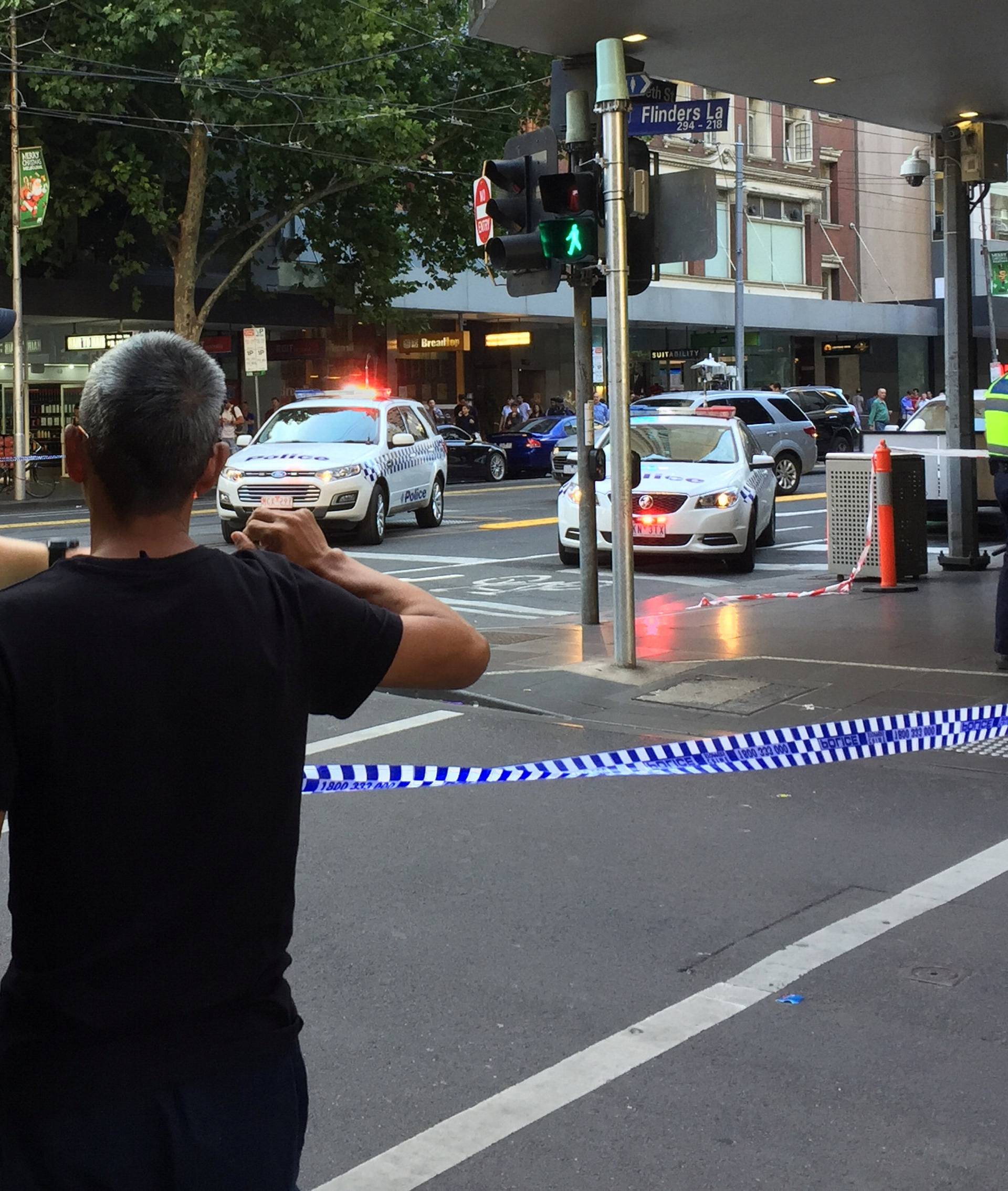 Police officers stand guard as members of the public stand behind police tape after the arrest of the driver of a vehicle that ploughed into pedestrians at a crowded intersection near the Flinders Street train station in central Melbourne
