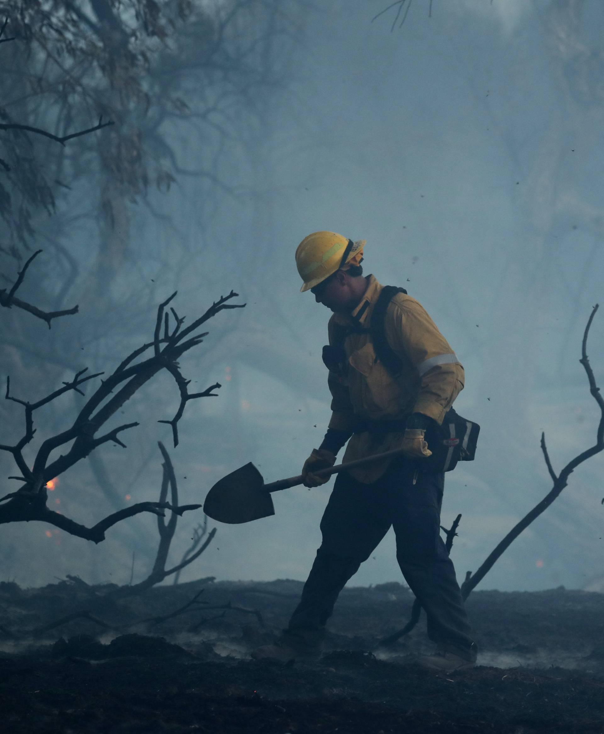 A firefighter works to put out hot spots on a fast moving wind driven wildfire in Orange, California