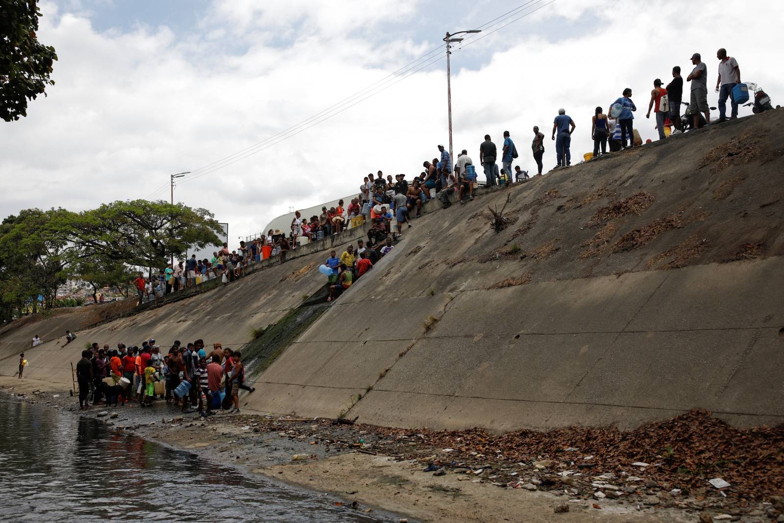 People gather to collect water released through sewage drain that feeds into the Guaire River in Caracas