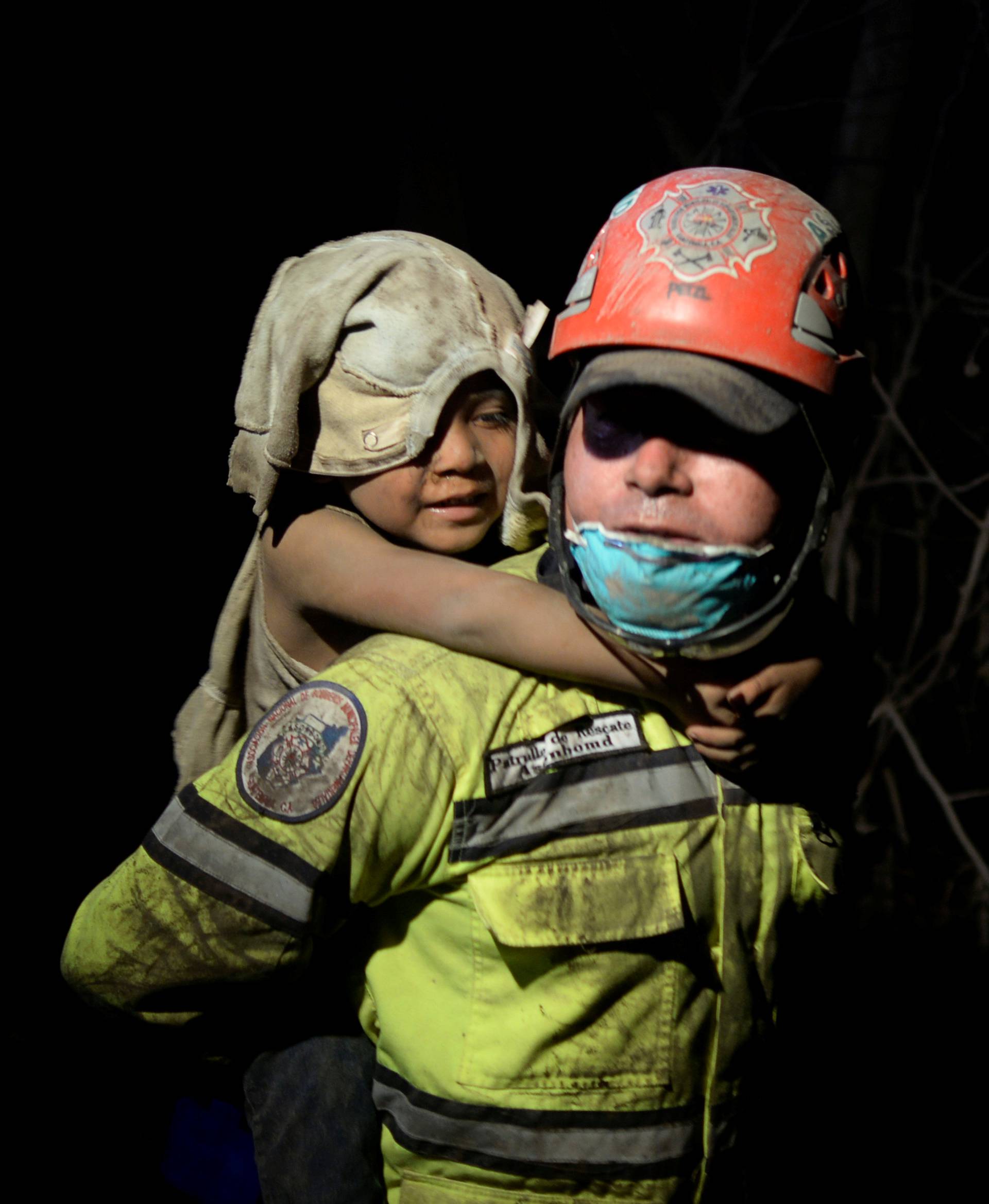A rescue worker carries a child covered with ash after Fuego volcano erupted violently in El Rodeo