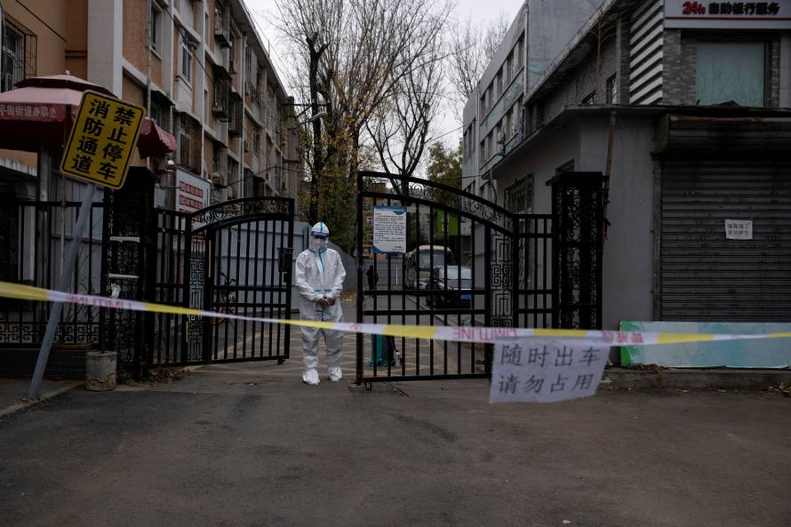 FILE PHOTO: An epidemic-prevention worker in a protective suit stands guard at the gate of a residential compound as coronavirus disease (COVID-19) outbreaks continue in Beijing