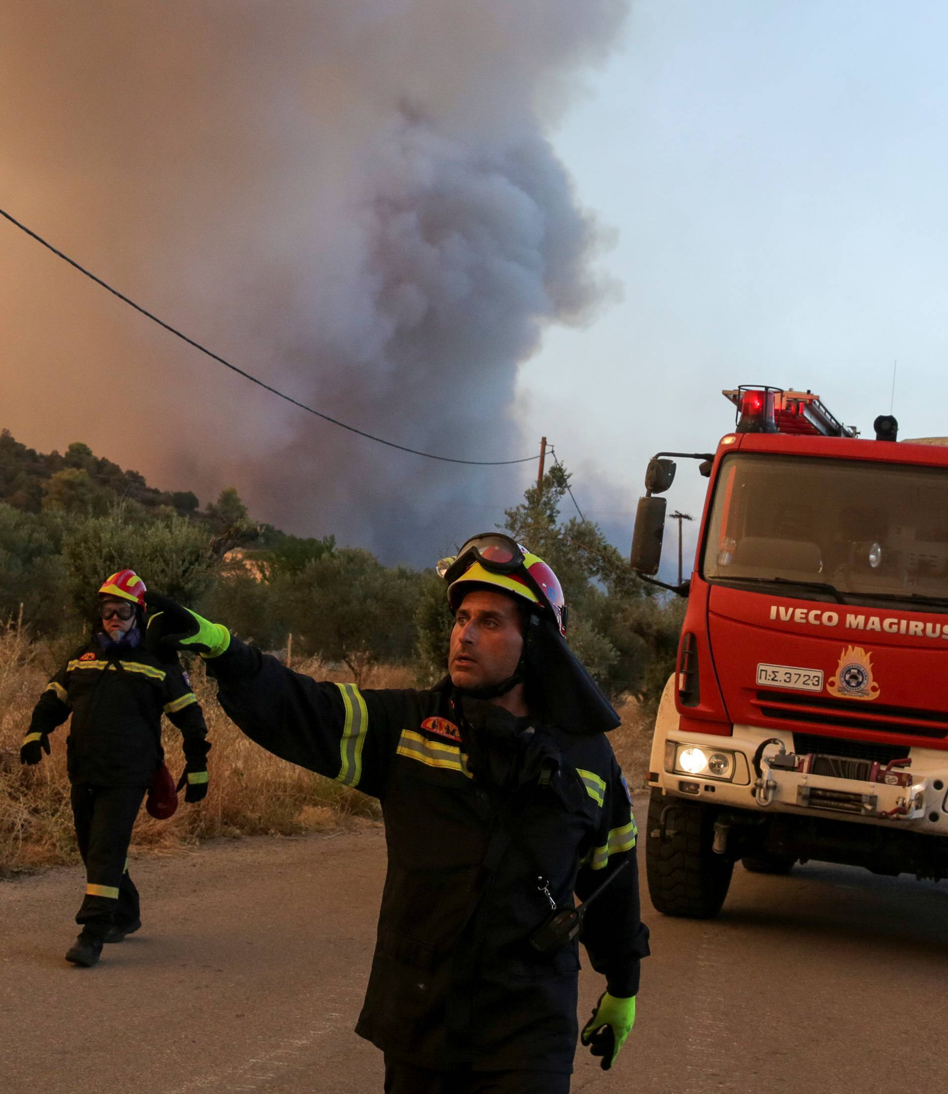 A firefighter gives directions as a wildfire burns near the village of Makrimalli on the island of Evia