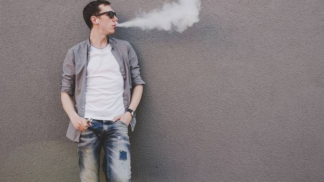 Young man smoking, vaping electronic cigarette or vape. Gray background