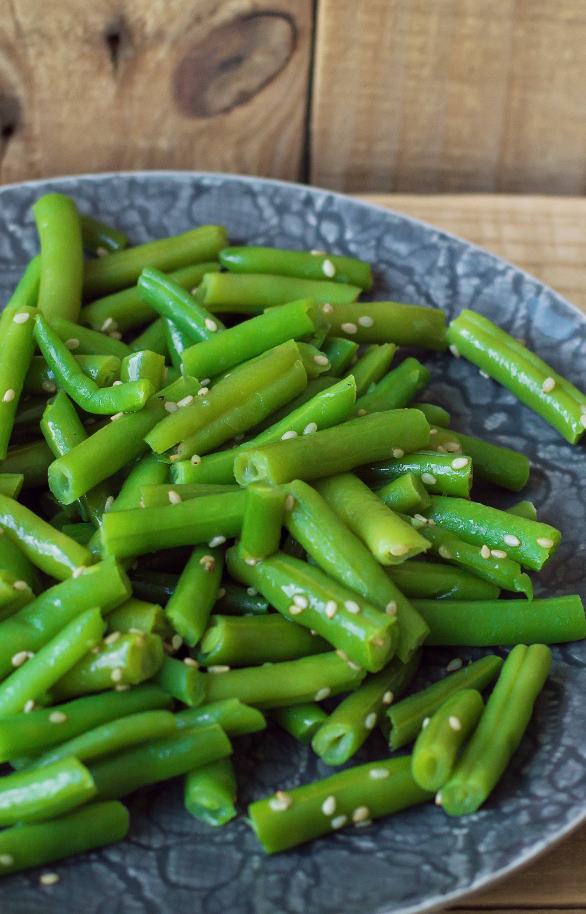 Plate with cooked green beans on wooden background