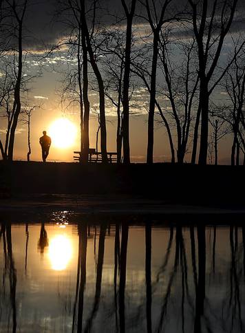 People stand and watch the sun set as they are reflected in a puddle at Presque Isle State Park in Erie, Pennsylvania