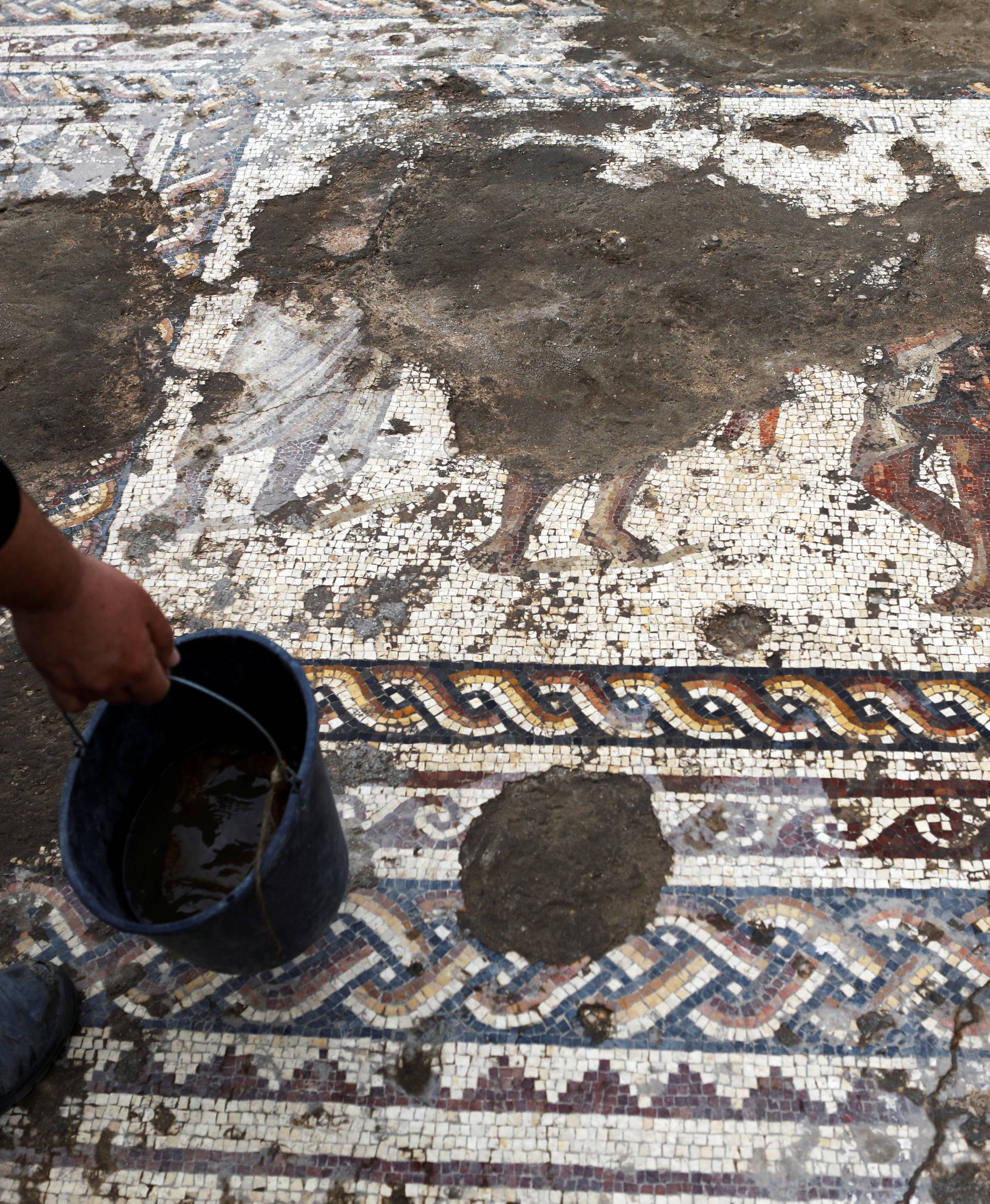 An Israel Antiquities Authority worker holds a bucket while cleaning a mosaic floor decorated with figures, which archaeologists say is 1,800 years old and was unearthed during an excavation in Caesarea