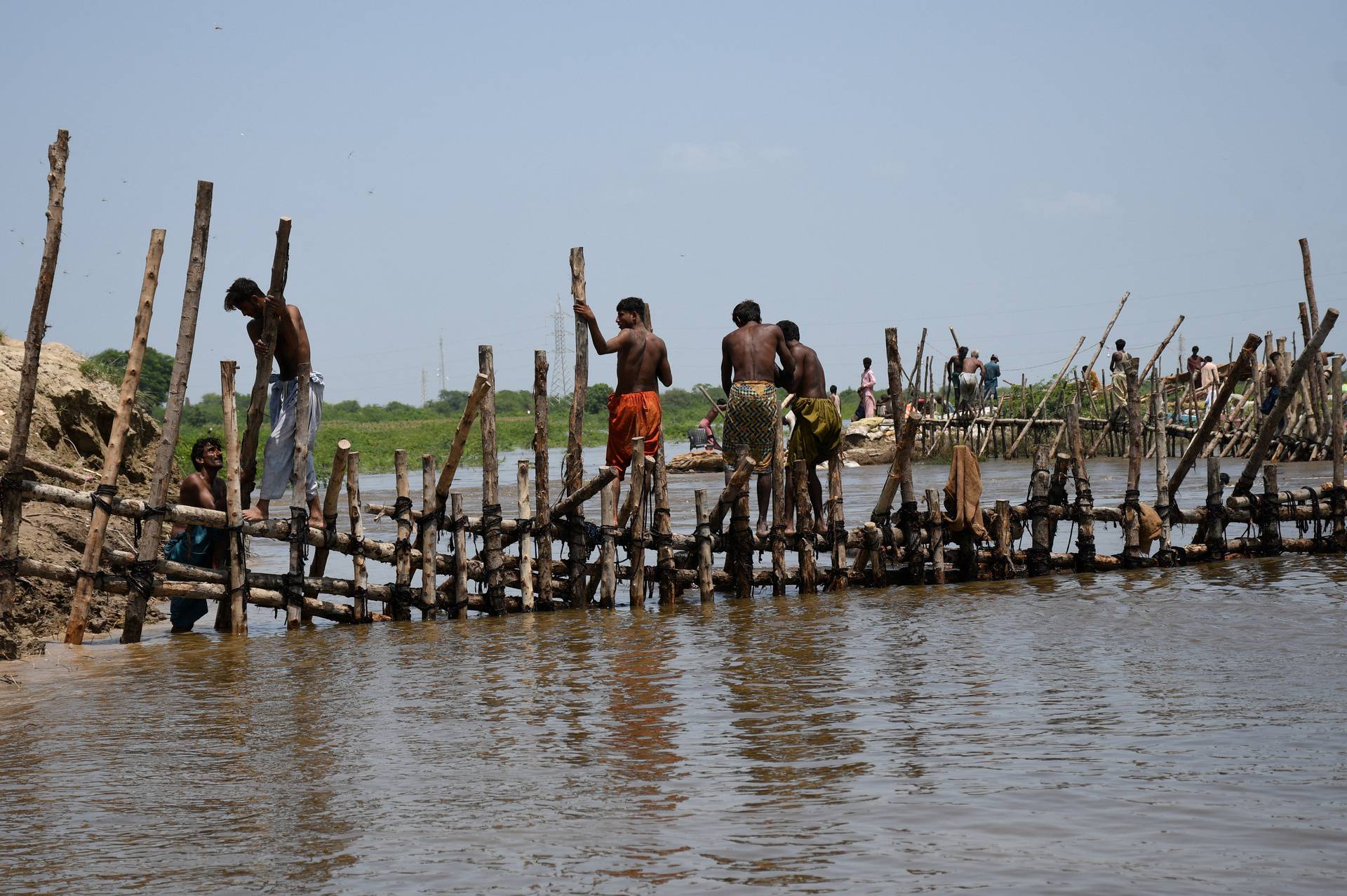 People prepare a barrier with wooden logs and sand bags to stop flood waters, following rains and floods during the monsoon season in Puran Dhoro, Badin