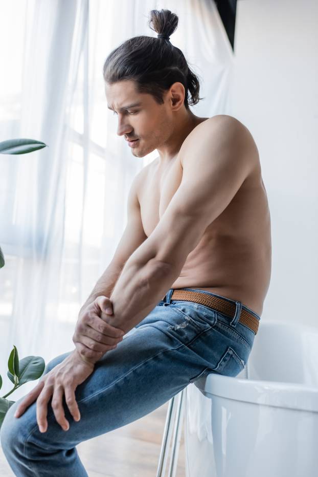 shirtless man with long hair sitting on white bathtub