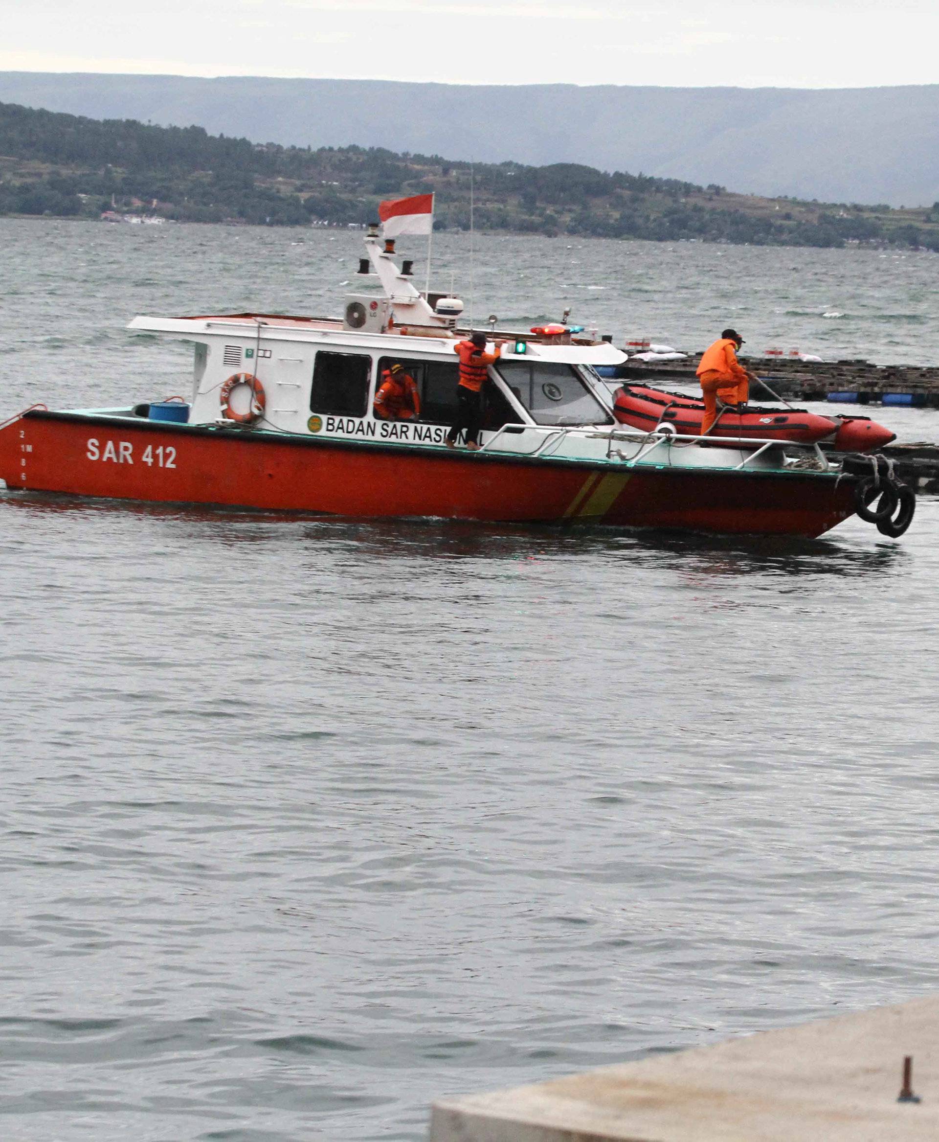 People watch a search and rescue boat used in the search for missing passengers on a ferry that sank in Lake Toba
