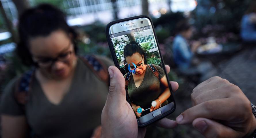 A Pokemon appears on the screen next to a woman as a man plays the augmented reality mobile game "Pokemon Go" by Nintendo in Bryant Park in New York City