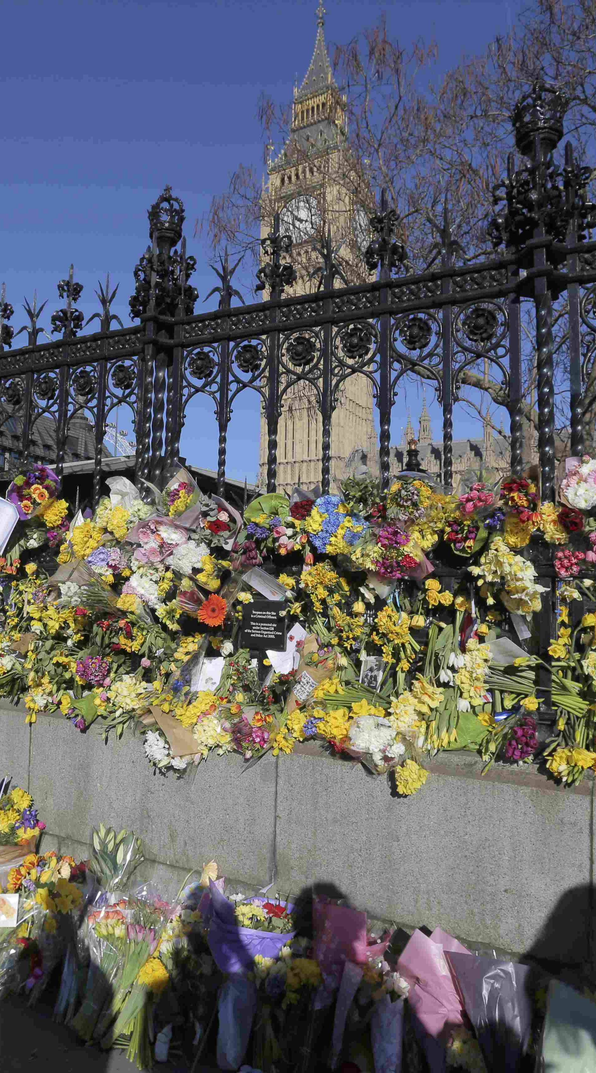 Onlookers view floral tributes on the wall surrounding the Houses of Parliament, following the attack in Westminster earlier in the week, in central London