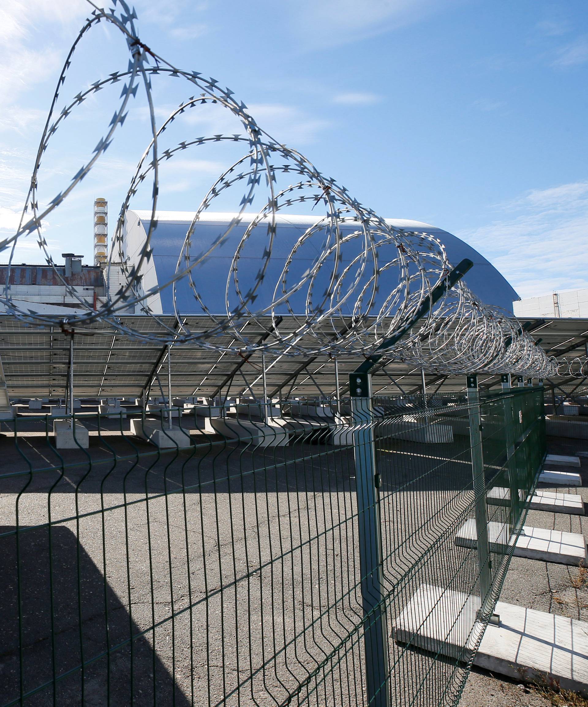 Solar panels are seen through barbed wire in front of the New Safe Confinement arch covering the damaged fourth reactor of the Chernobyl nuclear power plant, at a newly built solar power plant in Chernobyl