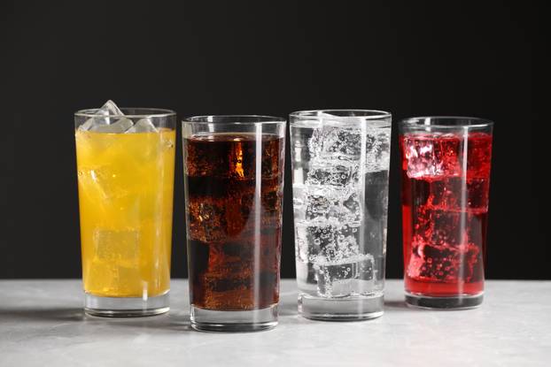 Glasses of different refreshing soda water with ice cubes on whi