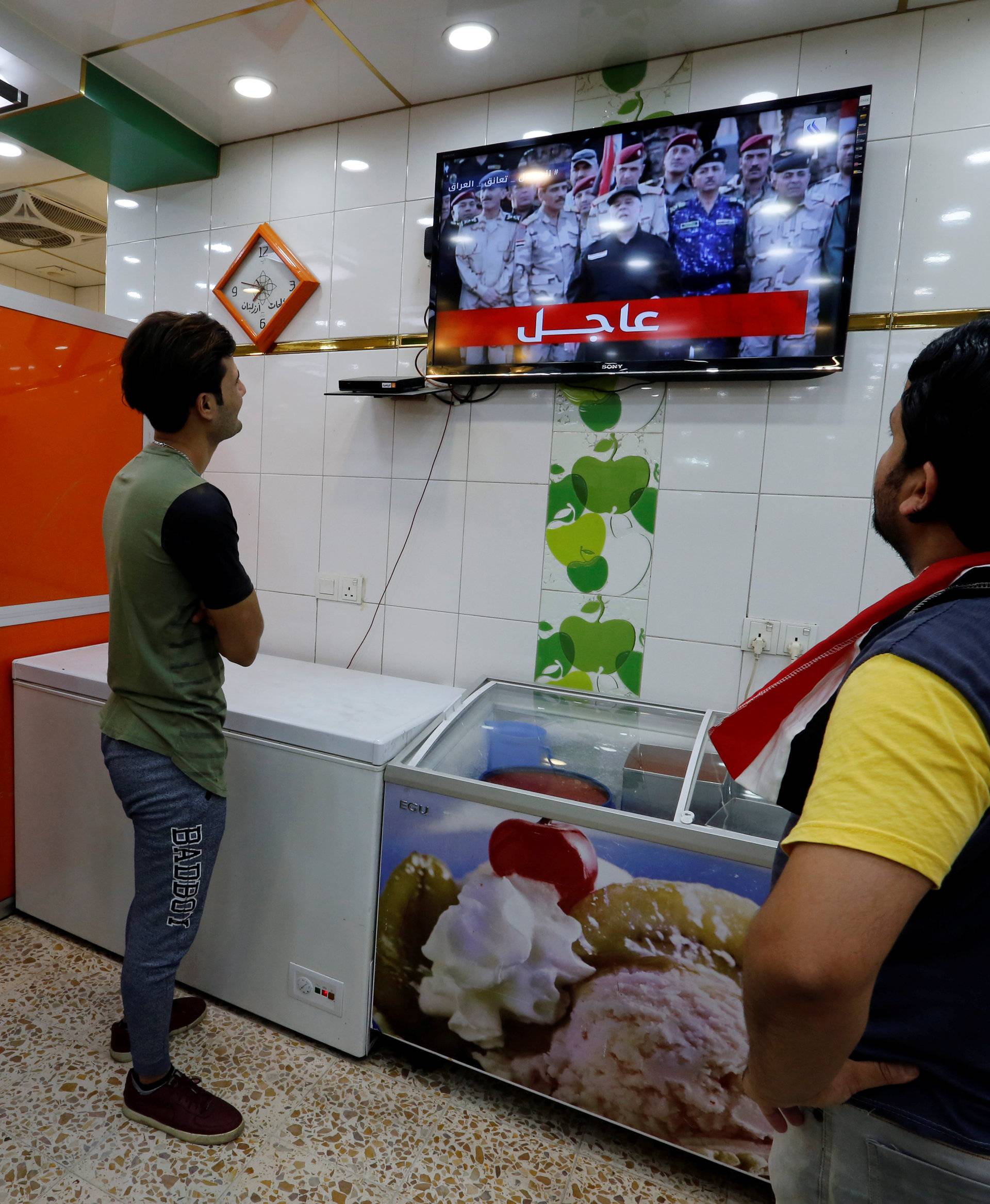 Iraqi men watch on a TV as Iraqi Prime Minister Haider al-Abadi announces victory over Islamic State, in Baghdad