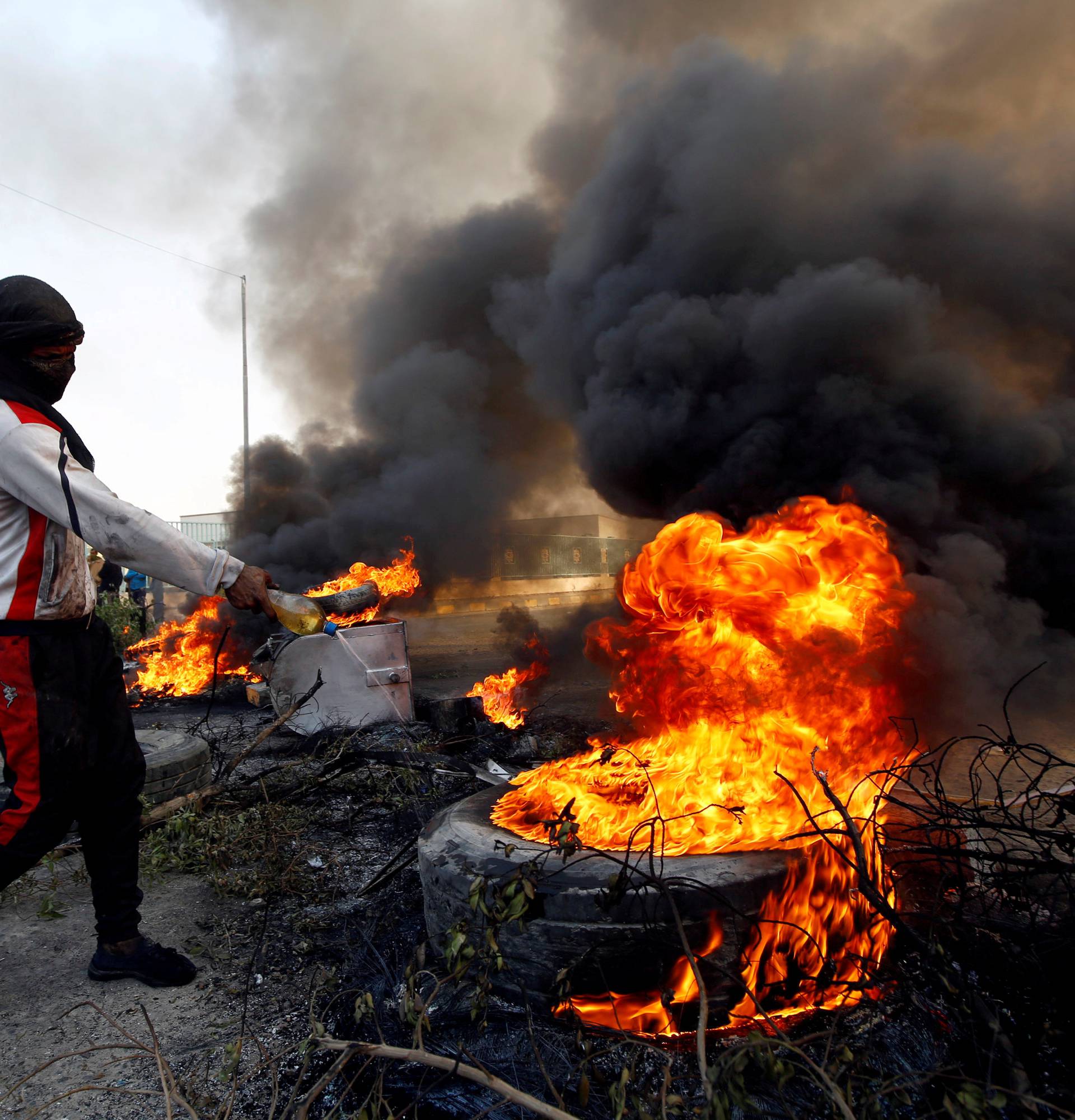 FILE PHOTO: Protester pours fuel on a tire to burn it as he blocks a street during ongoing anti-government protests in Najaf