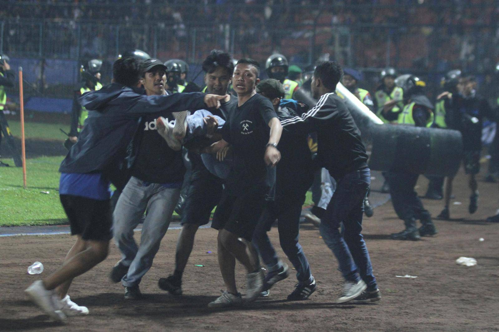 Supporters evacuate a man hit by tear gas fired by police during the riot after the league BRI Liga 1 football match between Arema vs Persebaya, in Malang
