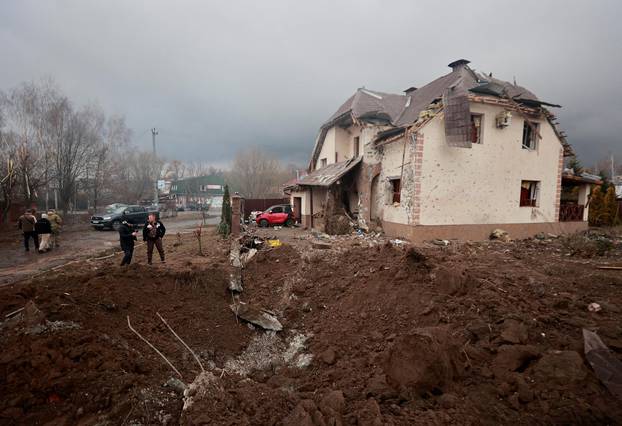 People stand next to a shell crater in front of a house damaged by recent shelling in the village of Hatne