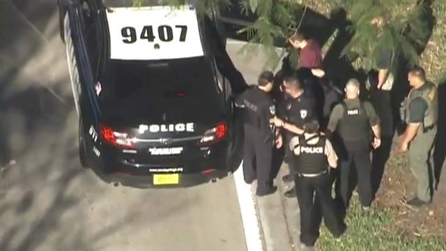 A man placed in handcuffs is led by police near Marjory Stoneman Douglas High School following a shooting incident in Parkland