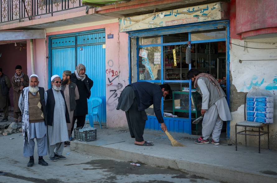 People remove shattered glass from their shop, following Pakistani airstrike, in the Darul Aman locality, in Kabul