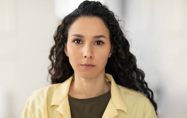 Portrait of focused young Latin woman in casual clothes looking at camera at home