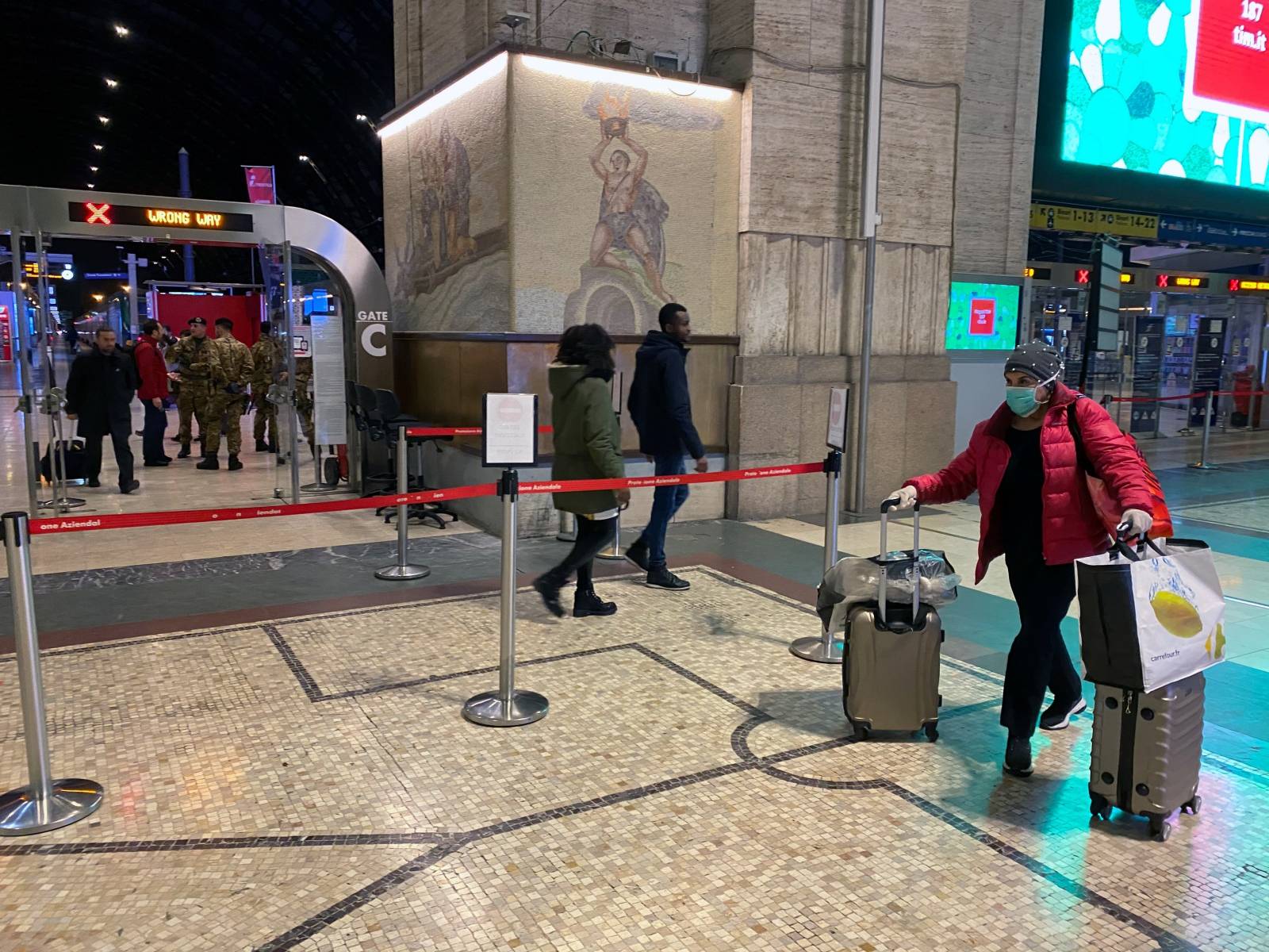 A woman wearing a protective face walks with her luggages inside Milan's main train station as Italian authorities prepare to lock down Lombardy to prevent the spread of the highly infectious coronavirus in Milan