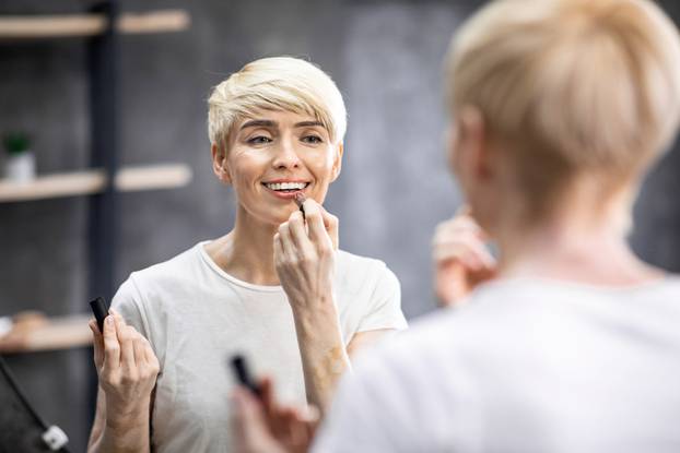 Middle-Aged Lady Applying Lipstick On Lips Standing In Bathroom