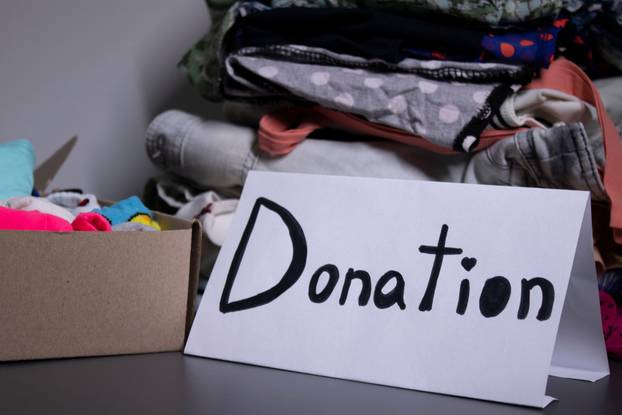 'donation' sign handwritten with black letters. A box with clothes and a pile of clothes nearby on a grey table.clothes donation concept. copy space