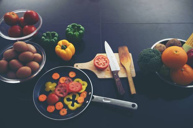 Food and fresh vegetables and salad bowls on kitchen table on to