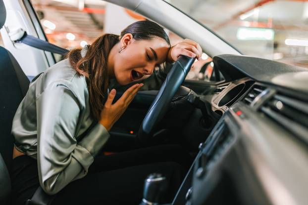 Young woman yawning in her car. Tired of driving around the park