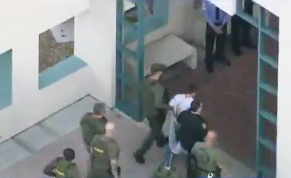 Police escort a suspect into the Broward Jail after checking him at the hospital following a shooting incident at Marjory Stoneman Douglas High School in Parkland