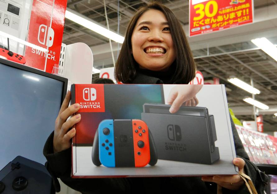 Nao Imoto smiles as she poses with her Nintendo Switch game console after buying it at an electronics store in Tokyo