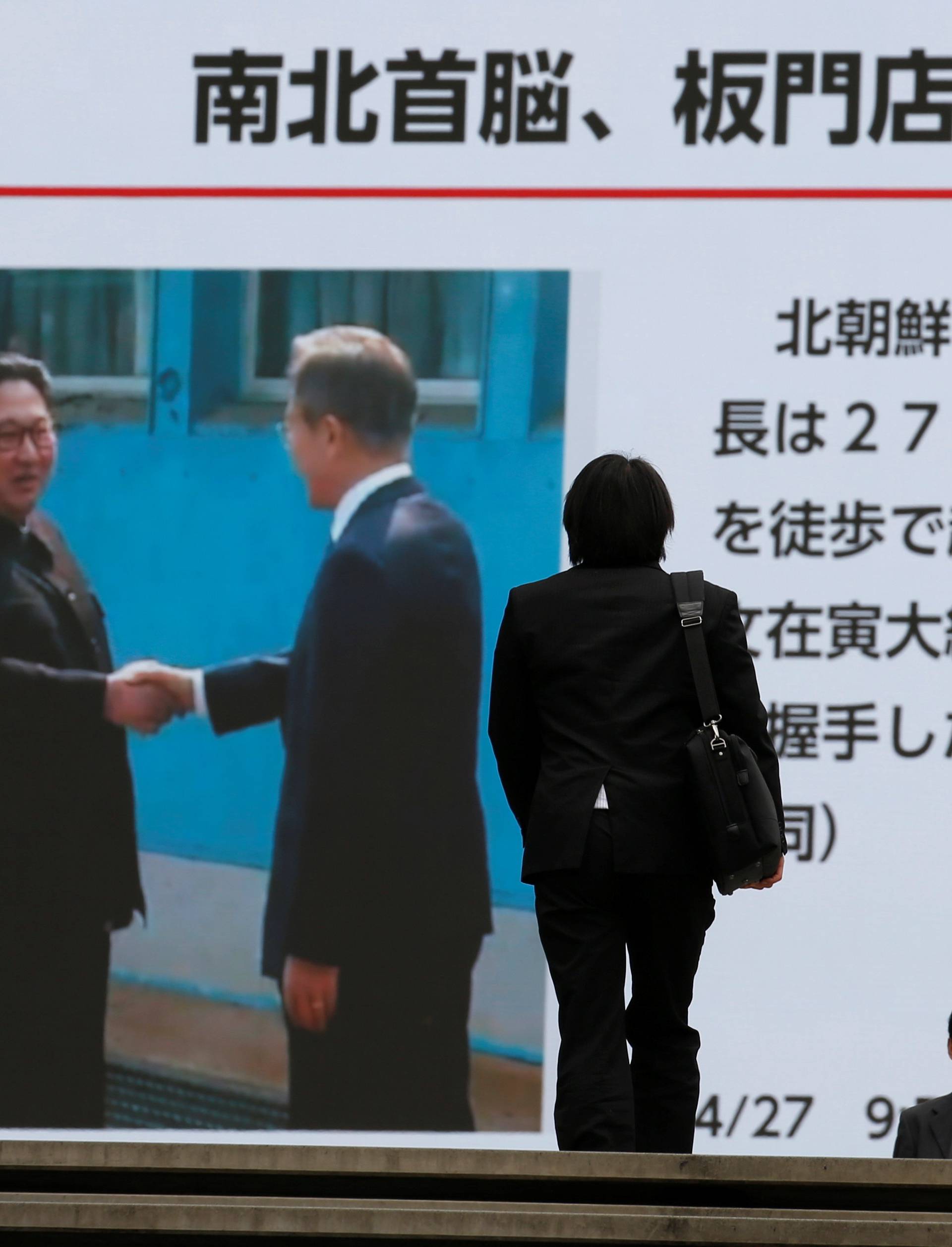 Passers-by walk in front of huge screen reporting the inter-Korean summit in Tokyo