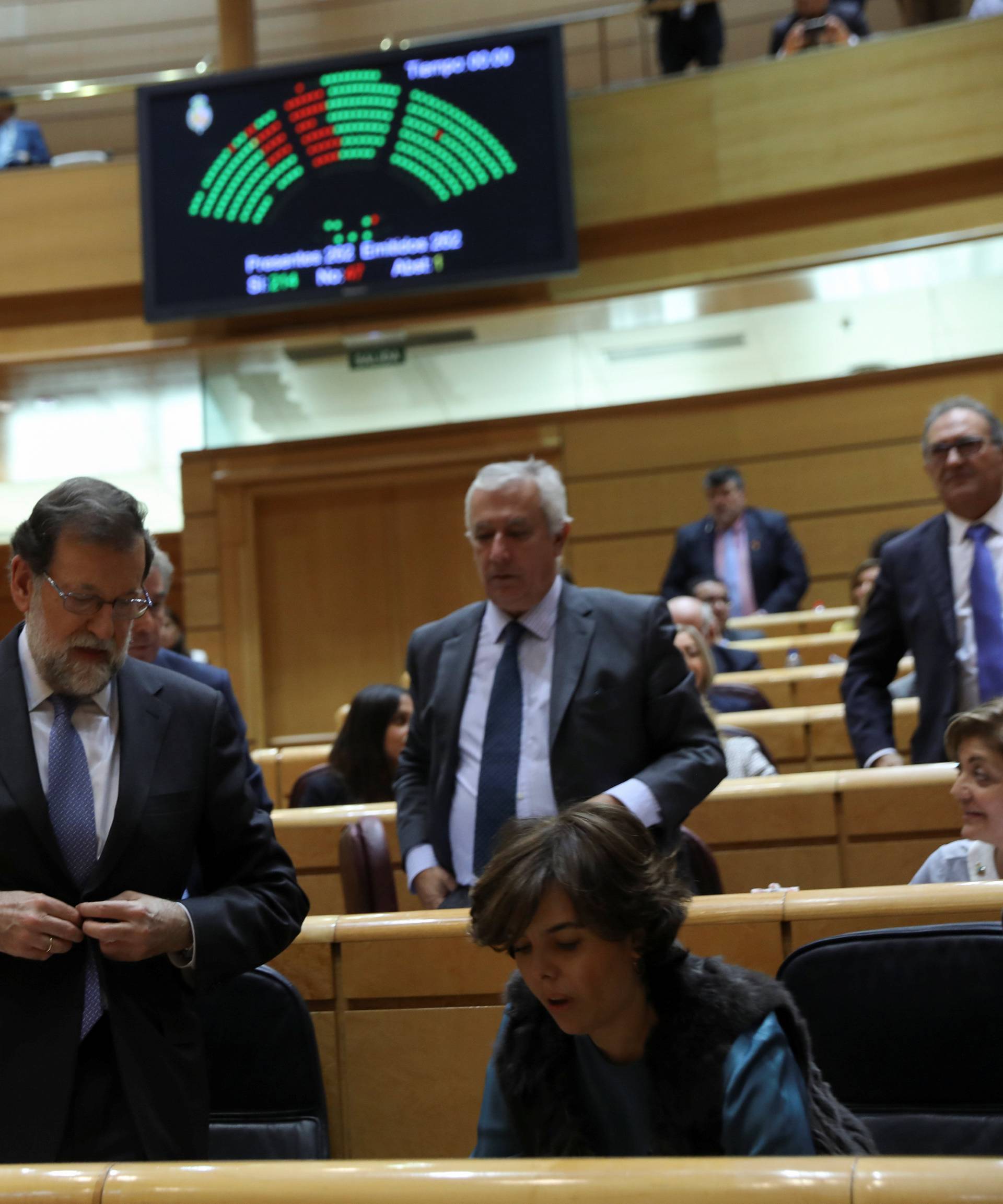 Spain's PM Rajoy and Deputy PM Saenz de Santamaria leave their seats as the results of a vote in the upper house Senate approving emergency measures to take control of the Catalan government are seen in a scoreboard in Madrid