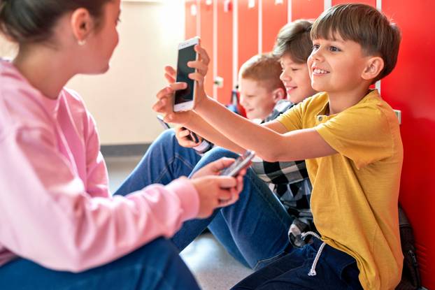 School children sitting on the floor and using smartphone
