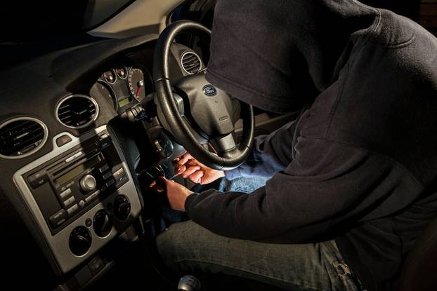 A hooded male hot wiring a car.