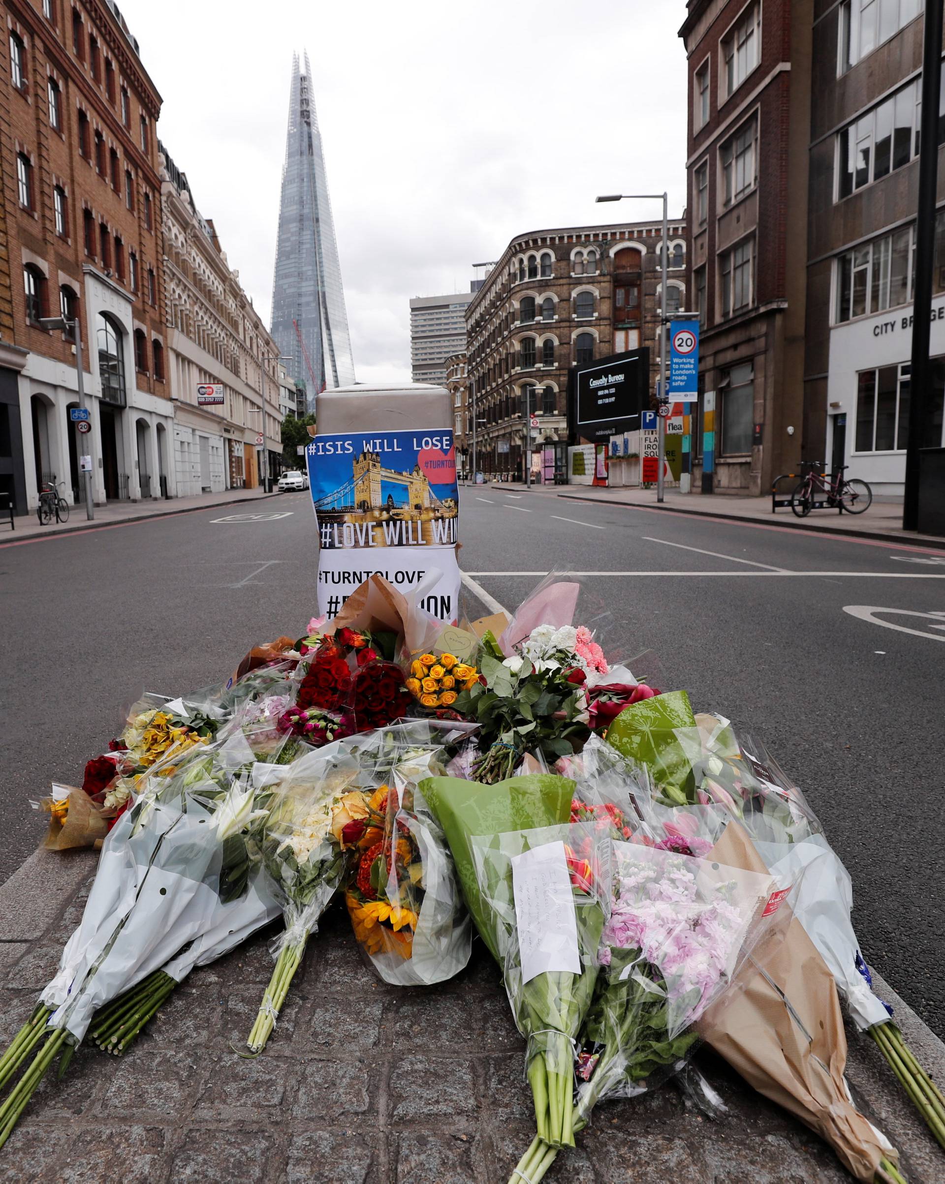 People stand around floral tributes on the south side of London Bridge near Borough Market after an attack left 7 people dead and dozens of injured in London