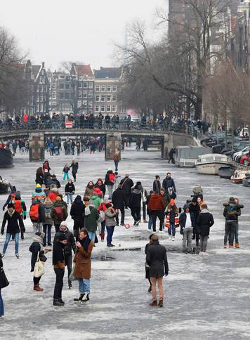 Ice skaters skate and walk on the frozen Prinsengracht canal during icy weather in Amsterdam