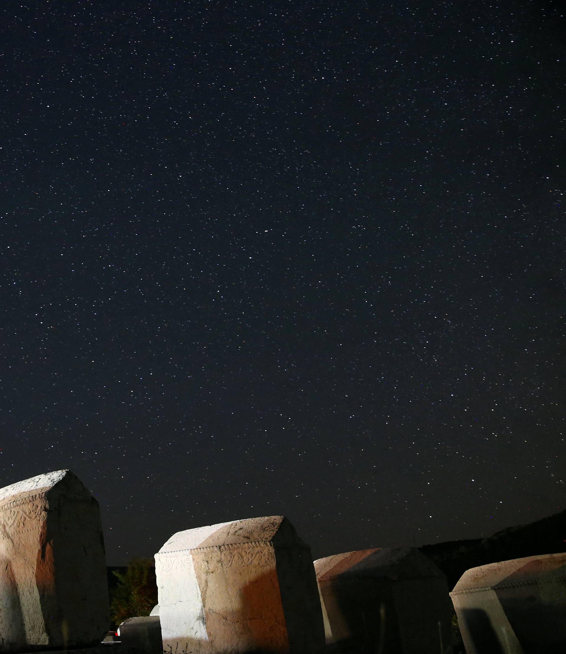 A meteor streaks past stars in the night sky above medieval tombstones in Radmilje near Stolac