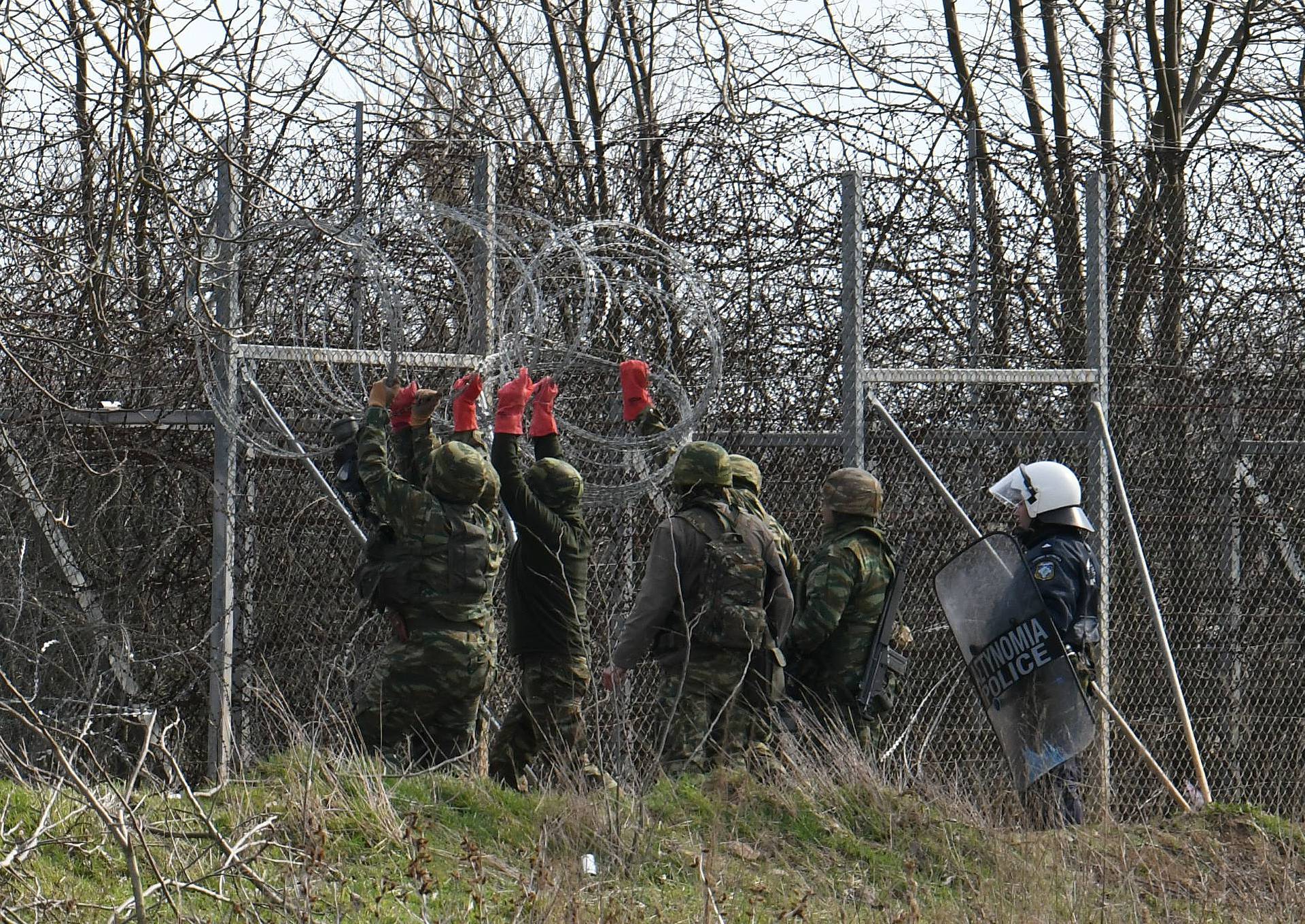 Greek soldiers reinforce the border fence with Turkey with barbed wire, as migrants who want to cross into Greece from Turkey's Pazarkule border crossing are gathered at the borderline, in Kastanies