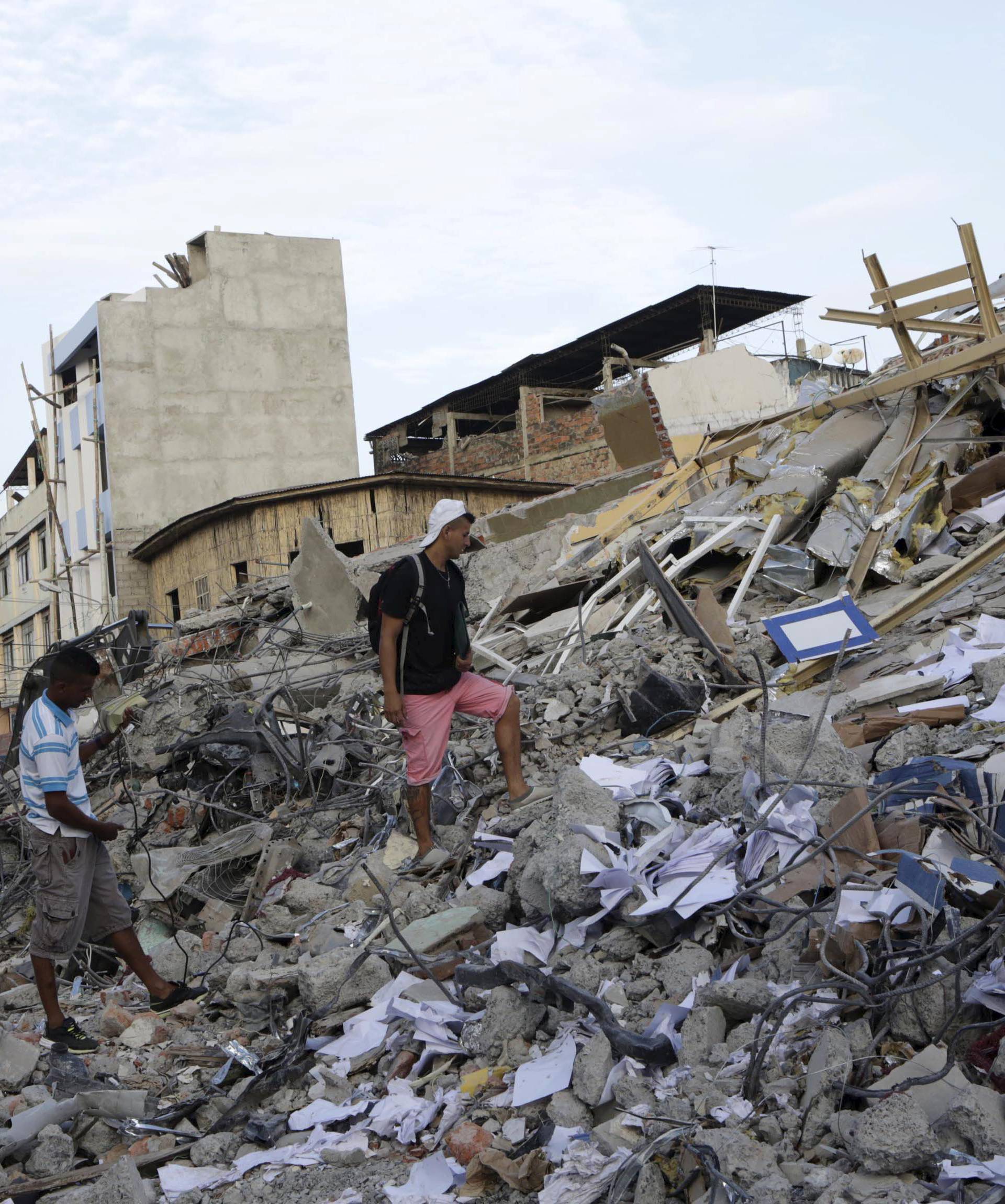 Residents walk on debris of a collapsed hotel after an earthquake struck off the Pacific coast, in Portoviejo, Ecuador