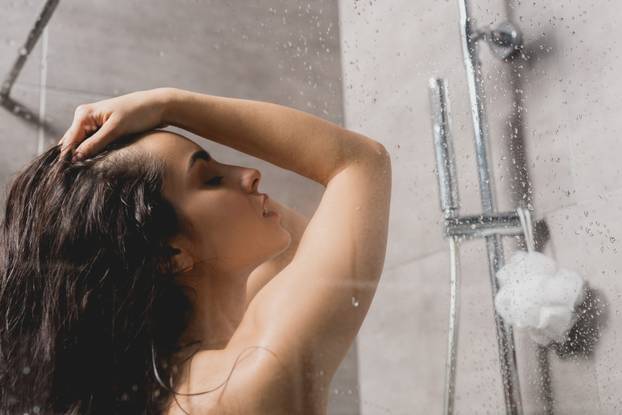 side view of attractive and brunette woman taking shower in cabin 