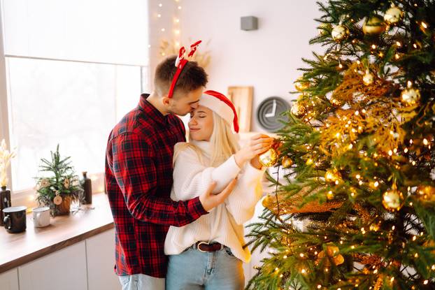 Happy couple decorating christmas tree at home. Smiling Man and Woman together Celebrating Christmas