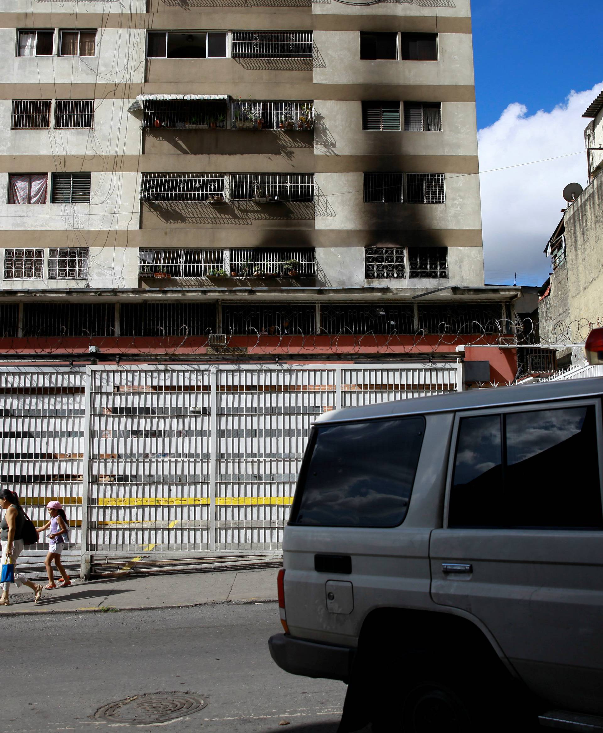 People walk past a building where damages are seen after an explosion in Caracas